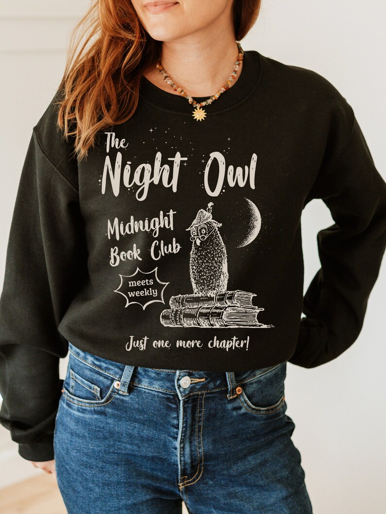 May include: Black sweatshirt with a white graphic of an owl wearing glasses and a hat, sitting on a stack of books. The text reads "The Night Owl Midnight Book Club meets weekly Just one more chapter!"