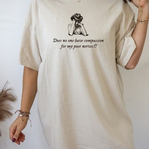 K&ouml;nnte beinhalten: Ein beigefarbenes Oversize-T-Shirt mit einer Vintage-Illustration einer Frau und dem Text "Does no one have compassion for my poor nerves?!"