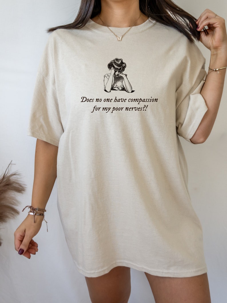 K&ouml;nnte beinhalten: Ein beigefarbenes Oversize-T-Shirt mit einer Vintage-Illustration einer Frau und dem Text "Does no one have compassion for my poor nerves?!"