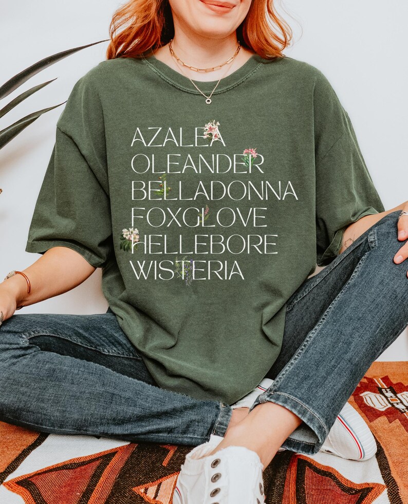 May include: A green t-shirt with a white graphic print of the words "Azalea", "Oleander", "Belladonna", "Foxglove", "Hellebore", and "Wisteria".