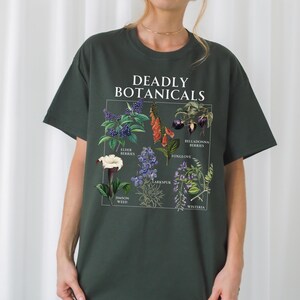 May include: Dark green t-shirt featuring a botanical illustration with the text "DEADLY BOTANICALS." The graphic includes images of elderberries, foxglove, and other plants. The word "forest" is printed at the bottom of the shirt.