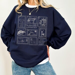 K&ouml;nnte beinhalten: Ein marineblauer Pullover mit einem grafischen Druck von Briefmarken mit verschiedenen Tieren und dem Text "The Marauders established 1971" und "Rule Breakers Mischief Makers".