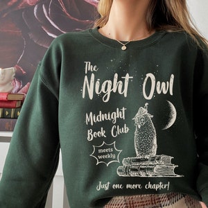 May include: A dark green sweatshirt with a white graphic design featuring an owl, books, and the text "The Night Owl Midnight Book Club meets weekly Just one more chapter!"