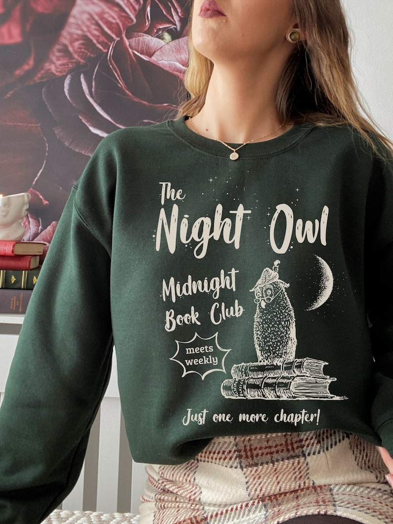 May include: A dark green sweatshirt with a white graphic design featuring an owl, books, and the text "The Night Owl Midnight Book Club meets weekly Just one more chapter!"