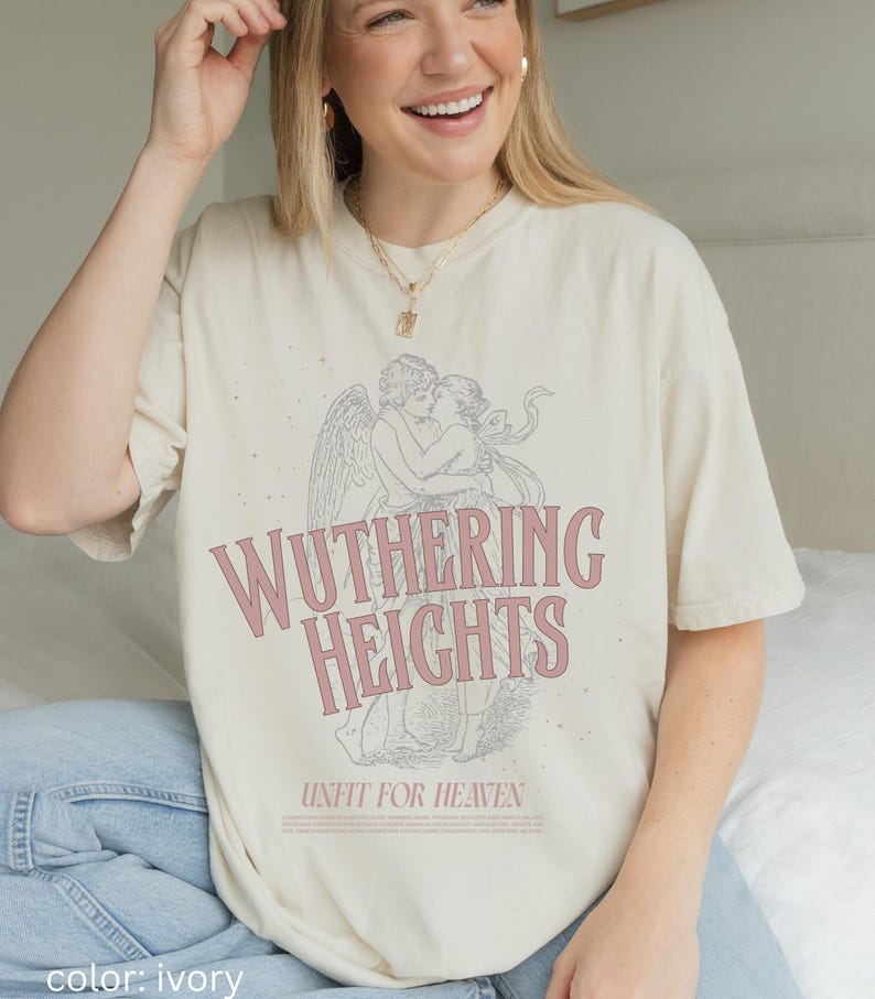 May include: Ivory-colored t-shirt featuring the text "Wuthering Heights" in pink, with an illustration of two figures embracing. The phrase "Unfit for Heaven" is printed below the title. The shirt is a relaxed fit.