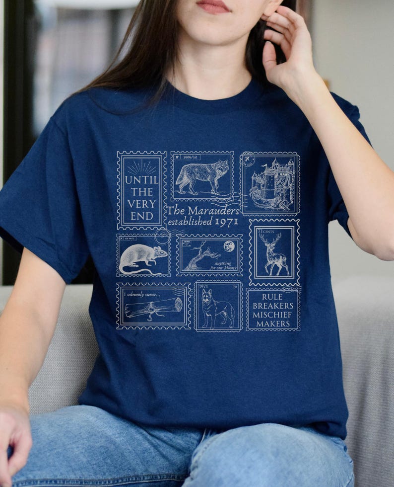 May include: A navy blue t-shirt with a white graphic print of stamps featuring illustrations of a wolf, a castle, a rat, a tree, a deer, a bone, and a dog. The stamps have text that reads "Until the very end", "The Marauders established 1971", "I solemnly swear...", "Rule breakers mischief makers".