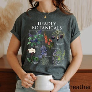 May include: Heather grey t-shirt featuring a botanical illustration with the text "DEADLY BOTANICALS". The graphic includes drawings of various plants such as Elderberries, Foxglove, and Jimson Weed. The shirt is a comfortable, casual style.