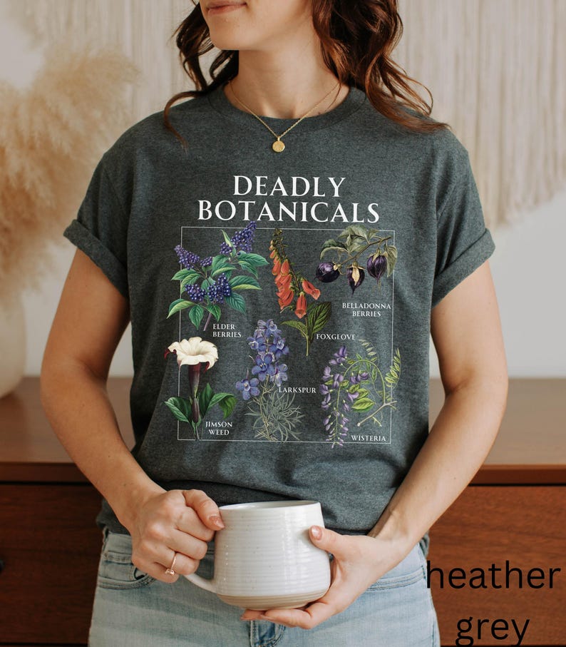May include: Heather grey t-shirt featuring a botanical illustration with the text "DEADLY BOTANICALS". The graphic includes drawings of various plants such as Elderberries, Foxglove, and Jimson Weed. The shirt is a comfortable, casual style.