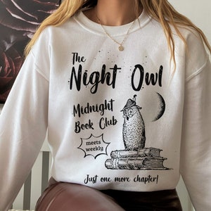 May include: White sweatshirt with black text that reads "The Night Owl Midnight Book Club meets weekly Just one more chapter!" and a black and white illustration of an owl wearing glasses sitting on a stack of books.