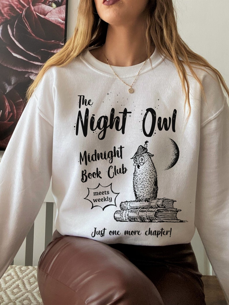 May include: White sweatshirt with black text that reads "The Night Owl Midnight Book Club meets weekly Just one more chapter!" and a black and white illustration of an owl wearing glasses sitting on a stack of books.