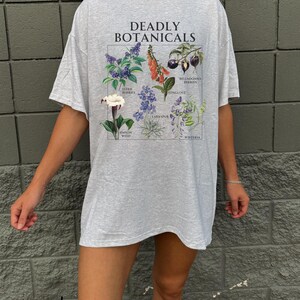 May include: Ash gray t-shirt with the text "DEADLY BOTANICALS" above a botanical illustration. The illustration features drawings of various plants, including Elderberries, Foxglove, and Wisteria. The shirt is a relaxed fit.