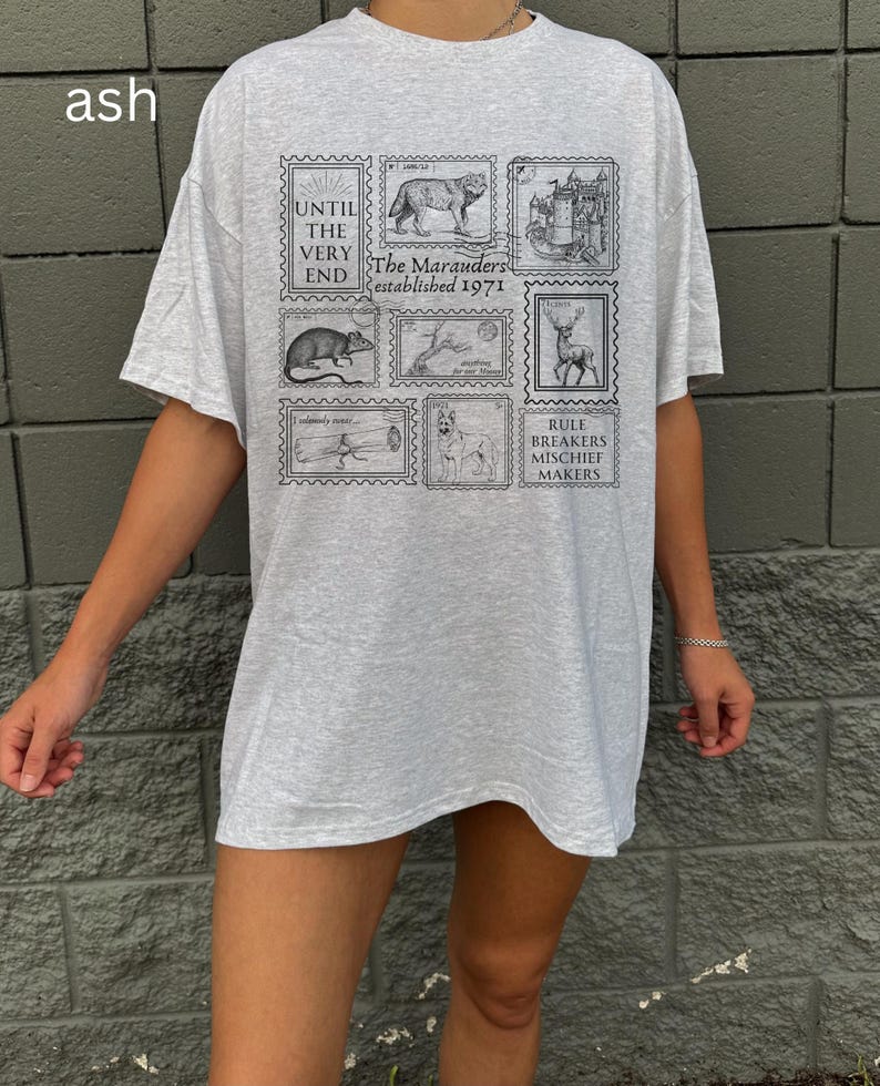 May include: A gray oversized t-shirt with a graphic print of black and white stamps. The stamps feature images of a wolf, a castle, a deer, a rat, a dog, and a log. The text on the stamps reads "Until the very end", "The Marauders established 1971", "Rule Breakers Mischief Makers".