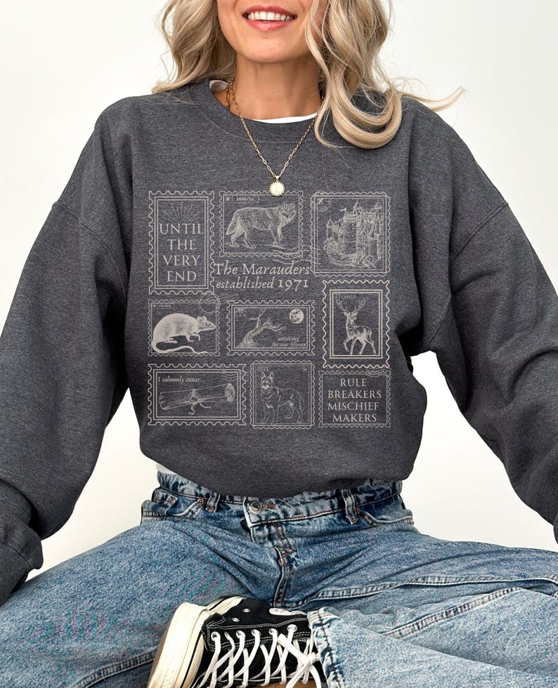 K&ouml;nnte beinhalten: Ein dunkelgraues Sweatshirt mit einem grafischen Druck von Briefmarken mit verschiedenen Bildern, darunter ein Wolf, eine Ratte, ein Reh und ein Schloss. Der Text auf den Briefmarken lautet "Until the very end", "The Marauders established 1971" und "Rule Breakers Mischief Makers".