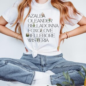 May include: White t-shirt with a black graphic print of the words "Azalea", "Oleander", "Belladonna", "Foxglove", "Hellebore", and "Wisteria".