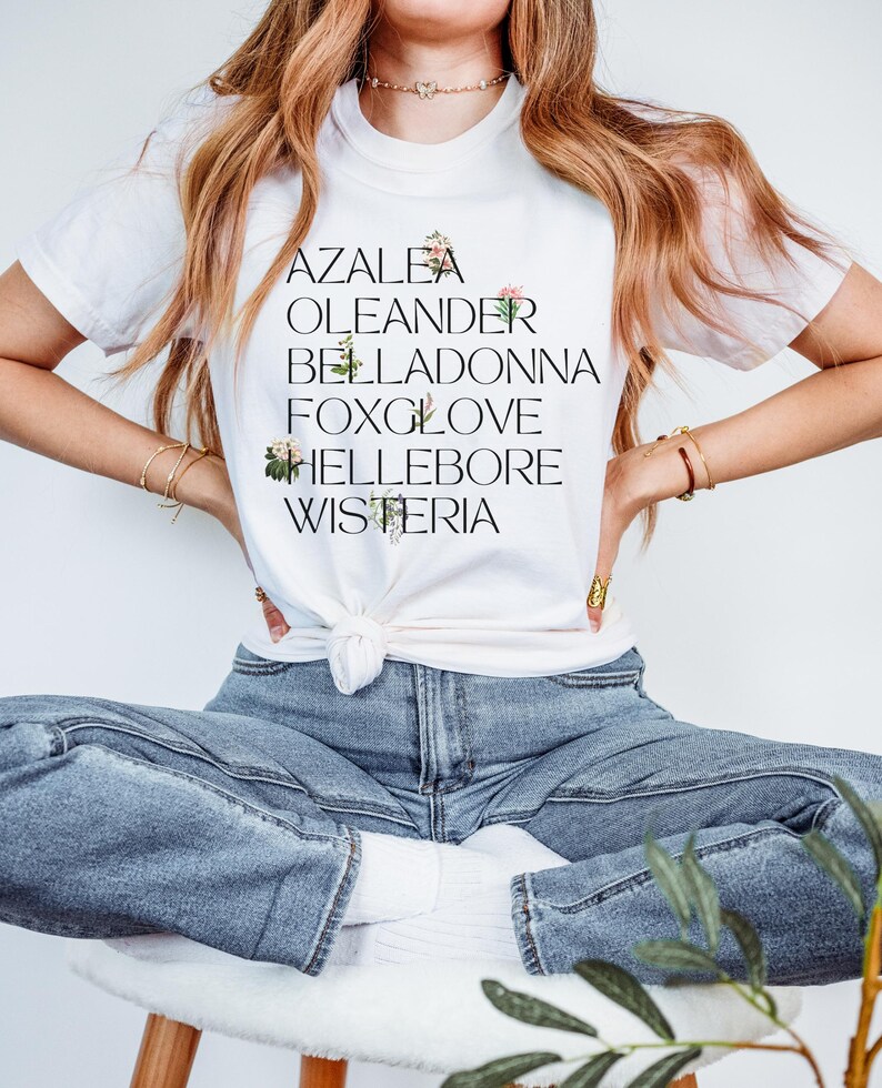 May include: White t-shirt with a black graphic print of the words "Azalea", "Oleander", "Belladonna", "Foxglove", "Hellebore", and "Wisteria".