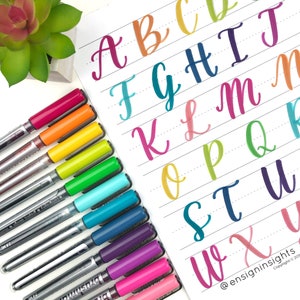 Peut inclure: Une feuille de papier avec l'alphabet &eacute;crit en cursive en diff&eacute;rentes couleurs. Les lettres sont &eacute;crites sur du papier lign&eacute;. Un ensemble de stylos color&eacute;s se trouve sur le c&ocirc;t&eacute; gauche de l'image.