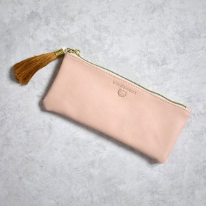 May include: A pale pink zippered pouch with a gold tassel. The pouch has the text "Bits & Baubles" printed on the front.