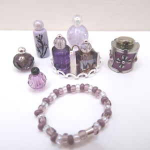 May include: An assortment of purple and clear glass perfume bottles and a beaded bracelet. The bottles vary in shape and size, with silver-colored lids and decorative elements. The bracelet features a mix of purple and clear beads.