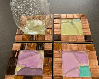 May include: Four square coasters with a mosaic design. Each coaster has a wooden border and a central mosaic of colored glass in shades of green, purple, and teal. A clear glass with bubbles sits on one coaster.