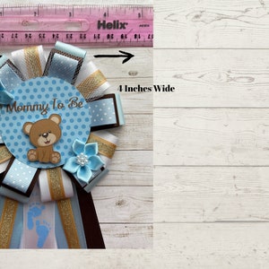 May include: A blue and white polka dot mommy-to-be sash with a brown bear and the text "Mommy To Be". The sash is 4 inches wide and has brown, white, and gold ribbons.