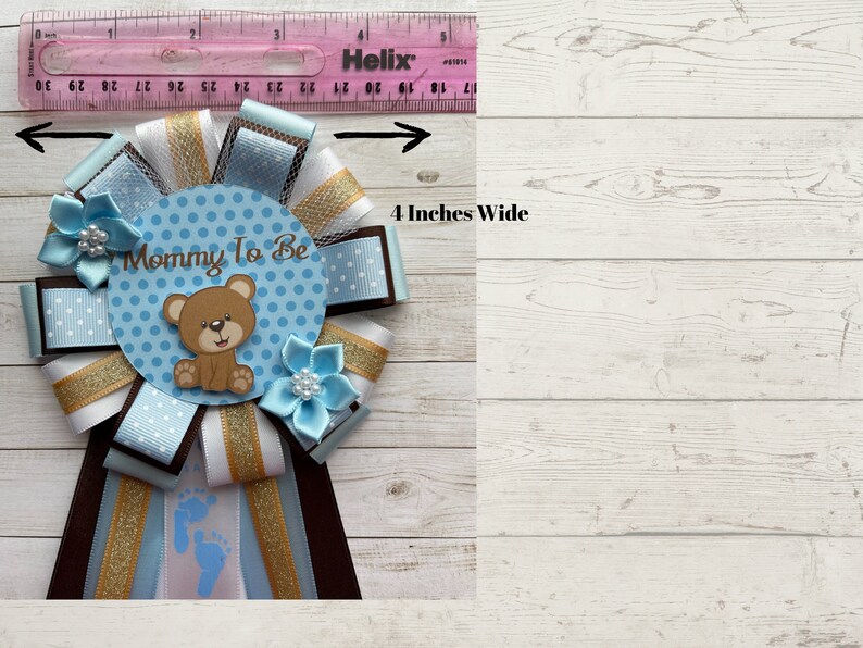 May include: A blue and white polka dot mommy-to-be sash with a brown bear and the text "Mommy To Be". The sash is 4 inches wide and has brown, white, and gold ribbons.