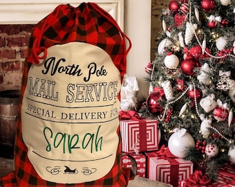 May include: Red and black plaid Christmas gift bag with a white circle that says "North Pole Mail Service Special Delivery for Sarah" with a green cursive name and a small illustration of a sleigh.