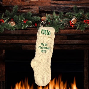 May include: A white knitted Christmas stocking with green embroidery that reads "Otto" and "My 1st Christmas 2023". The stocking is hanging from a fireplace mantel.