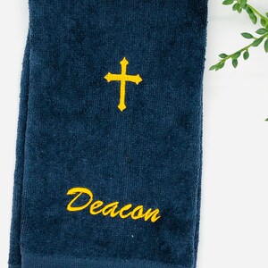 Puede incluir: Una toalla de mano azul oscuro con una cruz bordada en oro y el nombre "Deacon" en oro.