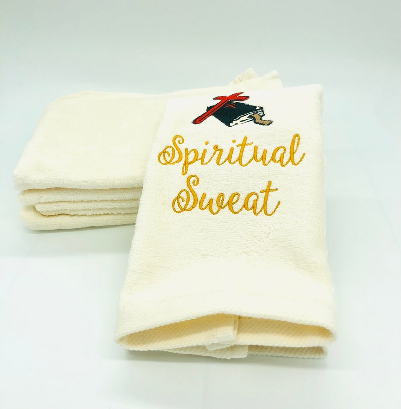 May include: A stack of white towels with gold embroidery that reads "Spiritual Sweat". A red and black illustration of a book and a wrench is above the text.