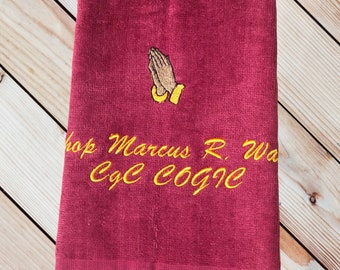 May include: Burgundy towel with a gold embroidered image of praying hands and the text "Bishop Marcus R. Walker C.Y.C. COGIC".