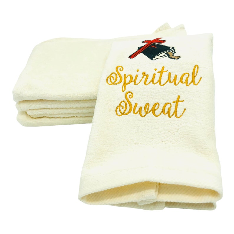 May include: A stack of white towels with an embroidered design. The design features a red cross and a book with the words "Spiritual Sweat" in gold lettering.