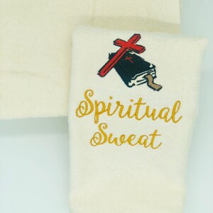 May include: White cotton hand towel with gold embroidery that reads "Spiritual Sweat" and a red cross over a black book.