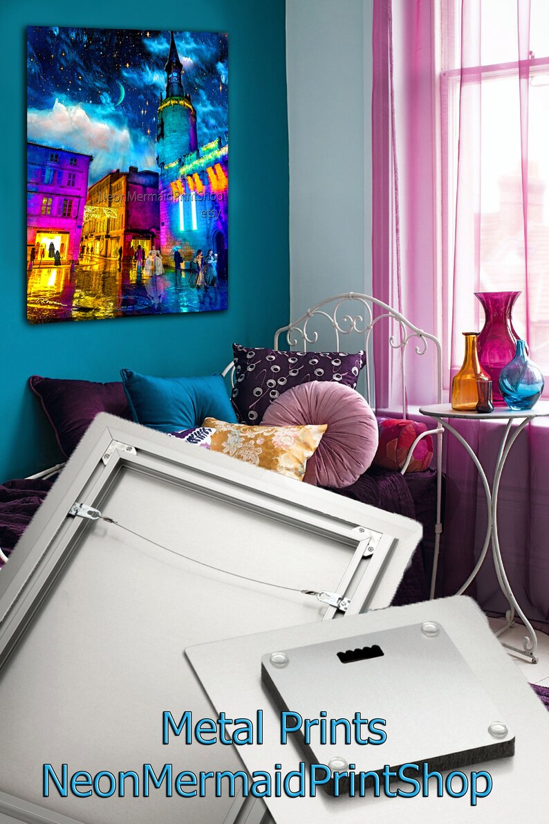 May include: A metal print of a colorful cityscape at night with a tall tower in the center. The print is framed with a silver frame and has a hanging wire on the back. The print is displayed on a white wall in a room with a bed and a window.