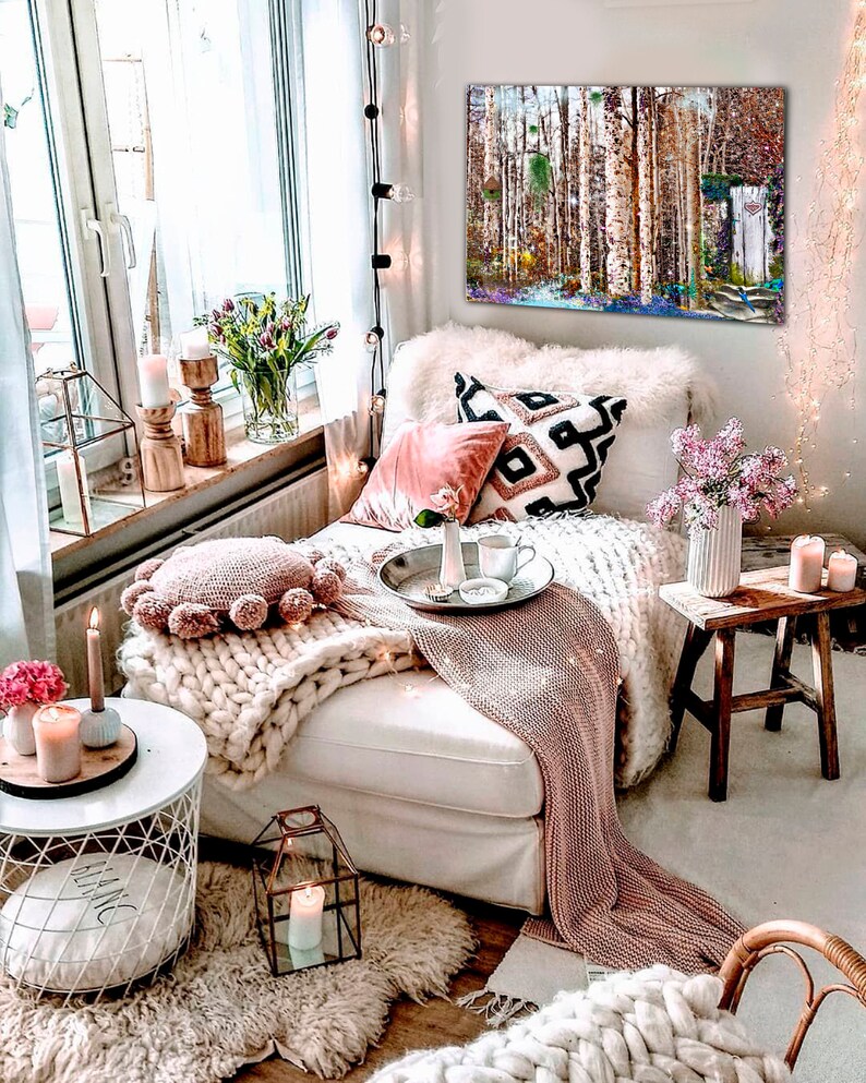 May include: A cozy living room with a white couch, a pink throw blanket, and a white knitted throw pillow. There is a painting of a birch forest on the wall, a small wooden stool, and a white side table with a candle on it. The room is decorated with fairy lights and flowers.