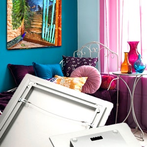 May include: Metal print showcasing a peacock image. The artwork presents a peacock on a stone wall, with a blue gate and stairs leading to a starry night scene. The print is displayed in a room with colorful decor.