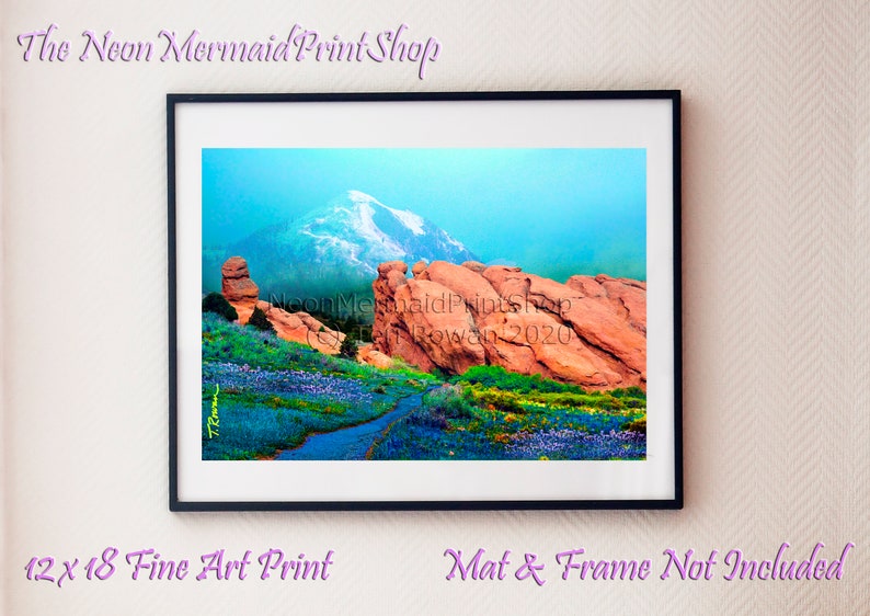 May include: A fine art print depicting a scenic landscape with a mountain range featuring snow-capped peaks, red rock formations, and a path leading through a field of wildflowers. The print is titled "The Neon Mermaid Print Shop" and is signed "Caden Rowan 2020".