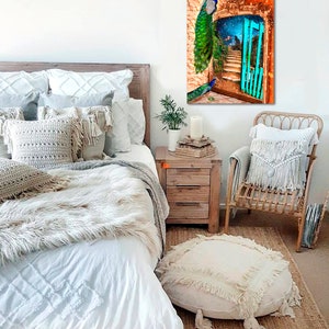 May include: A bedroom scene with a canvas print depicting peacocks and a turquoise gate. The room includes a wooden bed frame, white bedding, decorative pillows, a woven chair, and a round ottoman with fringe. The artwork is the focal point.