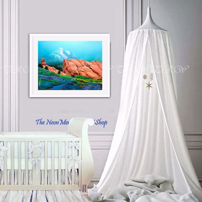 May include: A framed print of a colourful landscape with red rock formations, a blue sky, and a mountain in the background. The print is hanging on a wall in a nursery with a white cot and a white canopy.