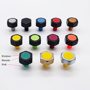 Op de afbeelding: Een verzameling zwarte, zeshoekige knoppen met verschillende gekleurde toppen en stelen. De toppen hebben kleuren als wit, blauw, rood, oranje, geel, groen en roze. De stelen zijn ook gekleurd, sommige metaal en sommige plastic.