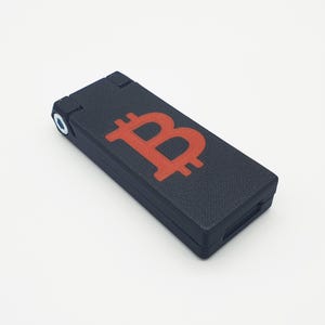 Könnte beinhalten: Ein schwarzes, rechteckiges, faltbares Etui mit einem roten Bitcoin-Symbol, das auf der Oberseite aufgedruckt ist.