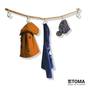 Può includere: Un filo per stendere i panni in corda con tre ganci appesi. Una felpa con cappuccio blu, una giacca marrone e un berretto a righe sono appesi ai ganci.