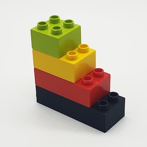 Könnte beinhalten: Ein Stapel aus vier bunten Lego-Steinen, beginnend mit einem grünen Stein, dann gelb, rot und schließlich schwarz.