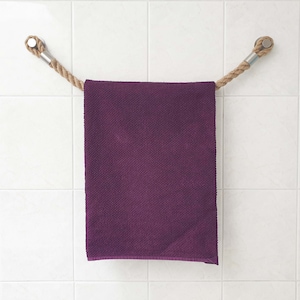 Può includere: Un asciugamano viola appeso a una corda con estremità in legno fissate al muro.