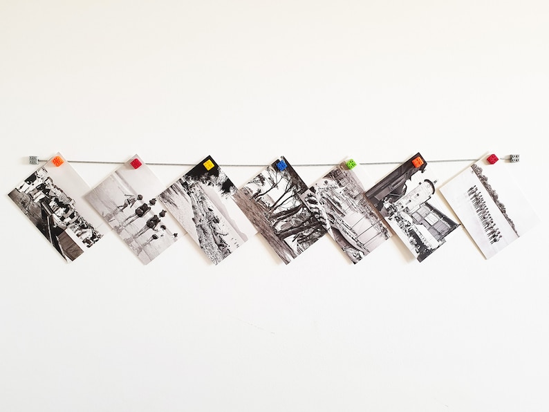 May include: A white wall with a string of black and white photos hanging from it. The photos are held in place by colorful plastic clips. The photos are all different sizes and shapes.