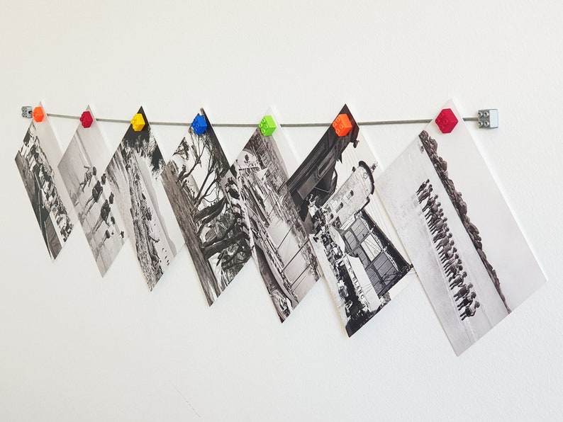 May include: A string of black and white photographs are hung on a white wall with colorful plastic clips. The photos are arranged in a staggered pattern.
