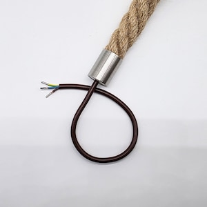 Puede incluir: Primer plano de una lámpara de cuerda marrón con un collar de metal. La cuerda es gruesa y texturizada, con un cable marrón y cables expuestos que se extienden desde la lámpara. El fondo es blanco.