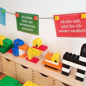 May include: A collection of colorful toy animals made from large plastic building blocks. The animals include a green turtle, a blue bird, a yellow duck, an orange and yellow fish, and a black and white zebra. The animals are arranged on a wooden shelf. The shelf is in front of a white wall with three signs hanging on a string. The signs have text in German. The text on the signs reads: "Hast Du Dir da Jammern selbst beigebracht, oder warst Du auf der Akademimimimi?", "ICH KANN TOTAL GUT MITMENSCHEN UMGEHEN!" and "Ich bin satt, jetzt bin ich wieder niedlich!"