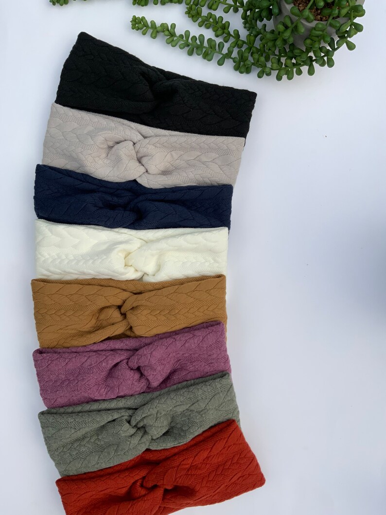 Puede incluir: Una pila de ocho diademas anudadas en varios colores, incluyendo negro, beige, azul marino, blanco, marr&oacute;n, morado, verde y rojo. Las diademas est&aacute;n hechas de una tela suave y texturizada.