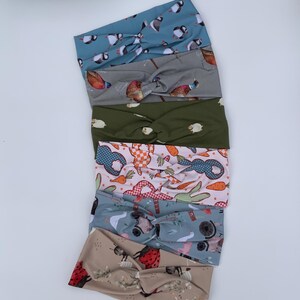 May include: Six fabric headbands with a twisted knot design. The headbands display patterns of birds, sheep, rabbits, and ladybirds. The colours are blue, grey, green, pink, and beige.
