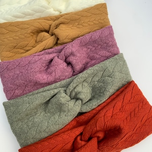 Puede incluir: Seis diademas de punto de diferentes colores con un patr&oacute;n de punto trenzado. Las diademas est&aacute;n apiladas una encima de la otra, con el color m&aacute;s oscuro en la parte superior y el color m&aacute;s claro en la parte inferior. Los colores son azul marino, blanco, marr&oacute;n, morado, verde y naranja.